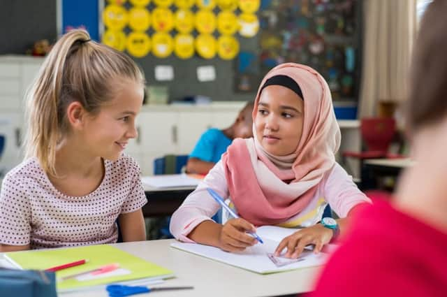 A young Arab girl with a hijab completes a school exercise with her best friend